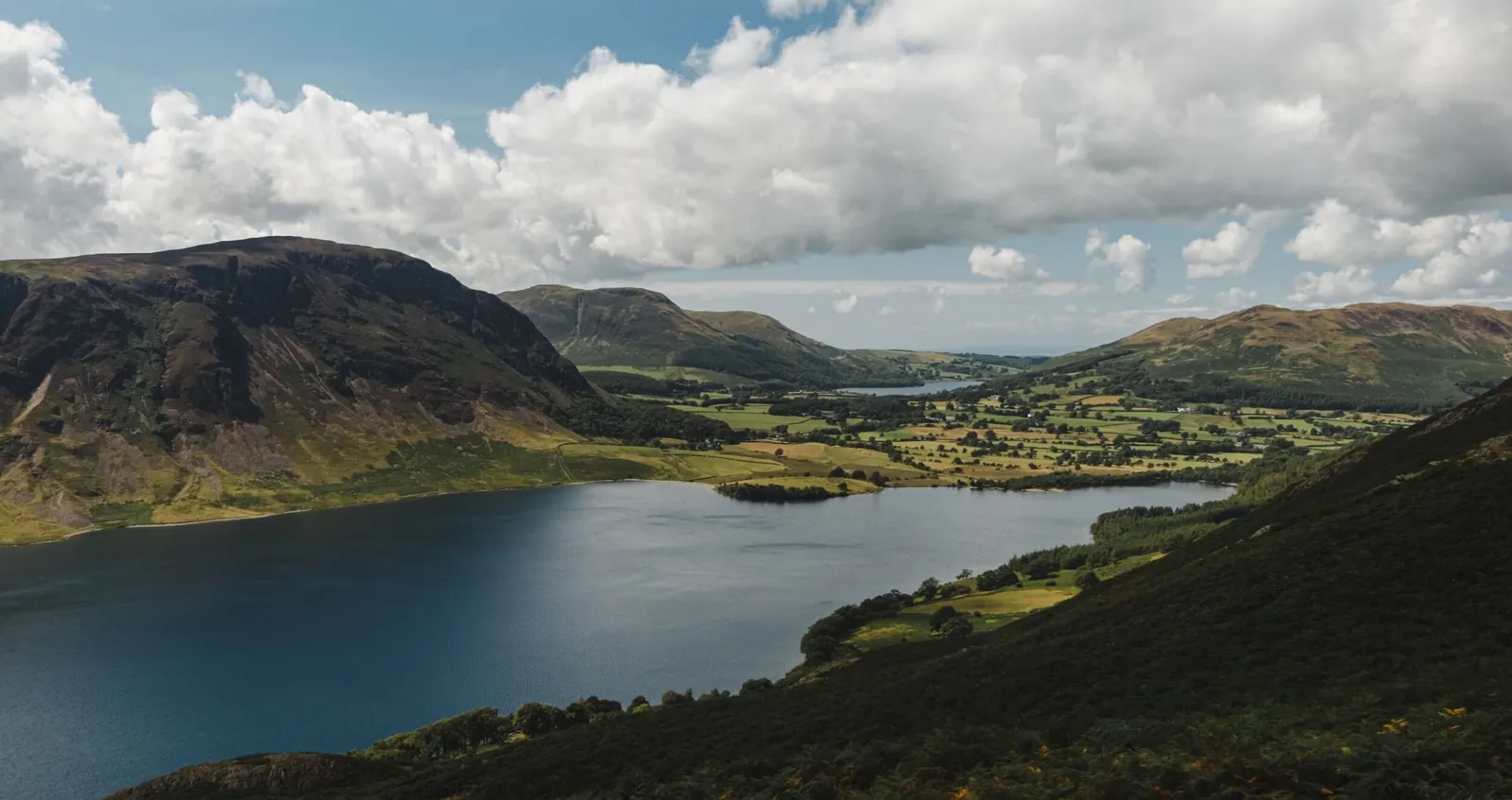 A lake surrounded by green fells and farmland in the Lake District, Cumbria